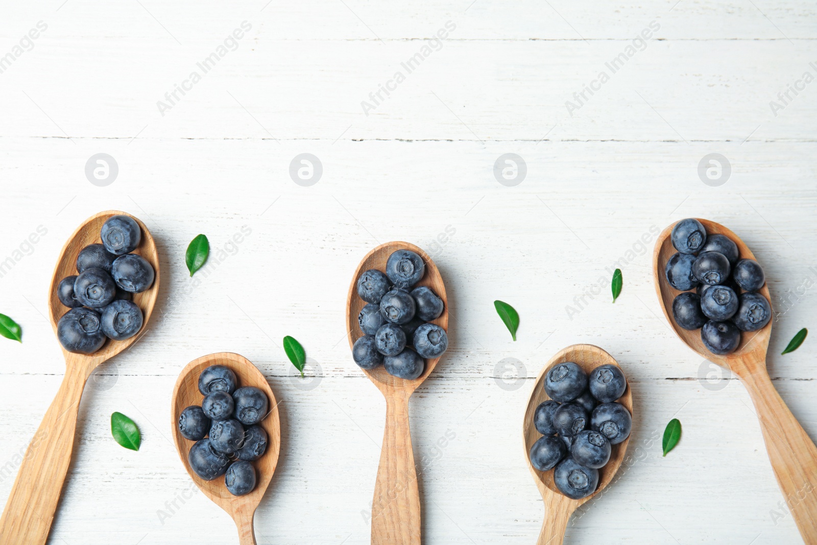 Photo of Flat lay composition of spoons with tasty blueberries and leaves on white wooden table, space for text