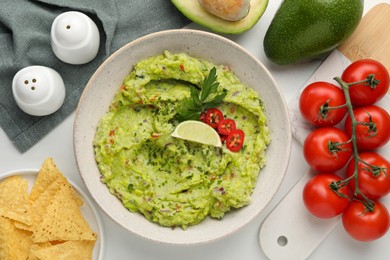 Delicious guacamole with nachos chips and ingredients on white table, flat lay