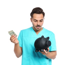 Photo of Portrait of young male doctor with piggy bank and money on white background
