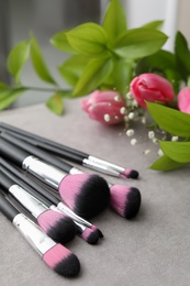 Makeup brushes and flowers on grey table