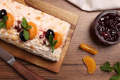 Photo of Tasty meringue roll with jam, tangerine slices and mint leaves on wooden table, flat lay