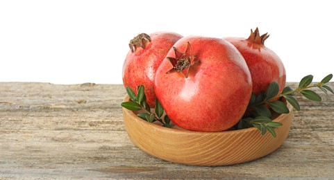 Photo of Fresh pomegranates and green leaves in bowl on wooden table against white background, space for text