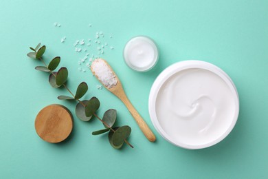 Photo of Moisturizing cream in open jars, sea salt and eucalyptus branch on turquoise background, flat lay. Body care products