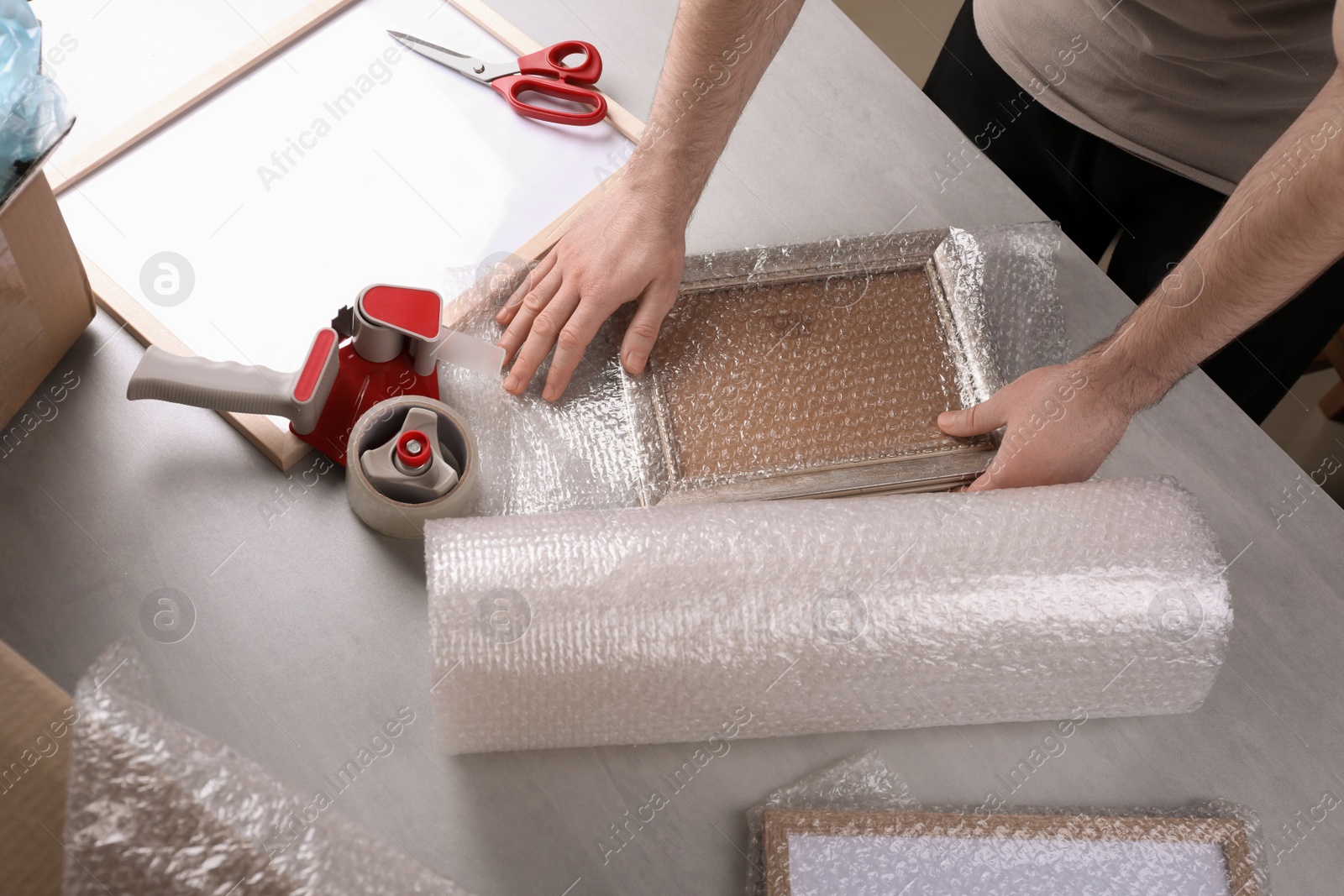 Photo of Man covering photo frame with bubble wrap at light grey table, closeup