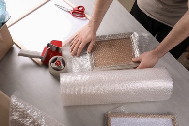 Photo of Man covering photo frame with bubble wrap at light grey table, closeup