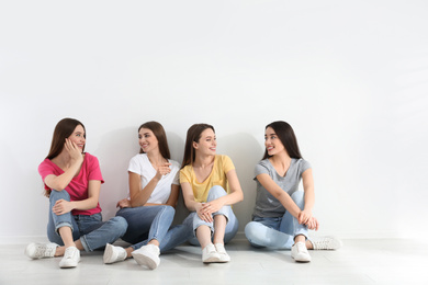 Photo of Beautiful young ladies in jeans and colorful t-shirts near white wall indoors. Woman's Day