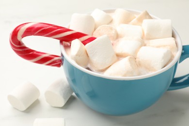 Tasty hot chocolate with marshmallows and candy cane on white marble table, closeup