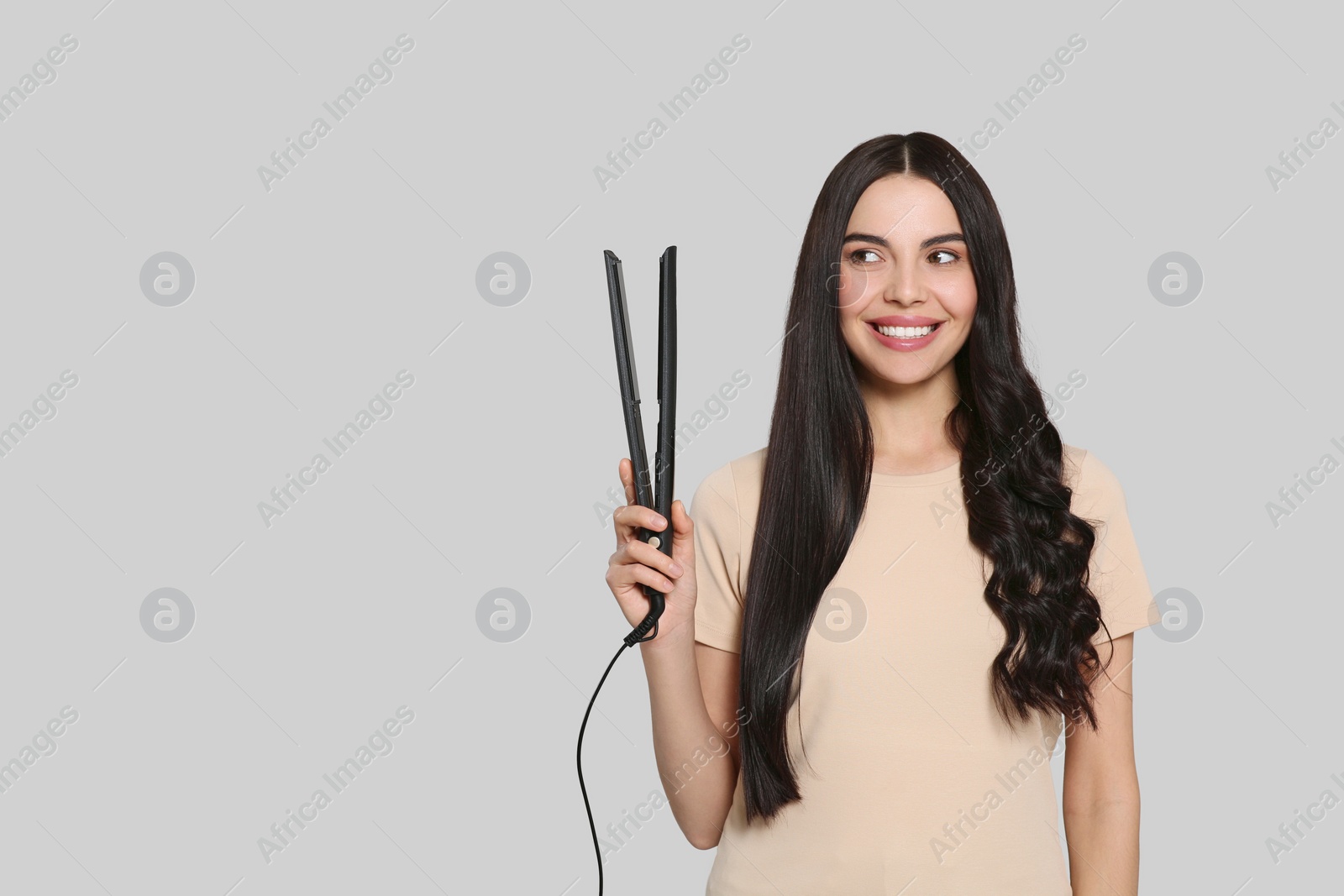 Photo of Beautiful happy woman with hair iron on light grey background. Space for text