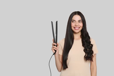 Beautiful happy woman with hair iron on light grey background. Space for text