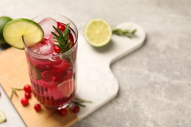 Photo of Tasty cranberry cocktail with rosemary and lime in glass on gray table, closeup. Space for text