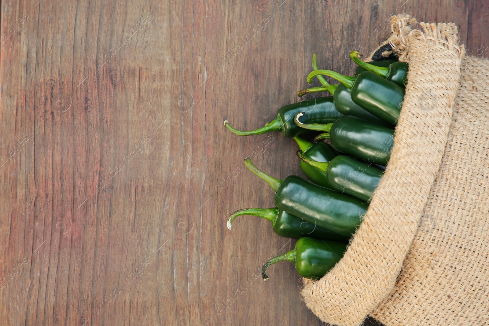 Photo of Sack with jalapeno peppers on wooden table, top view. Space for text