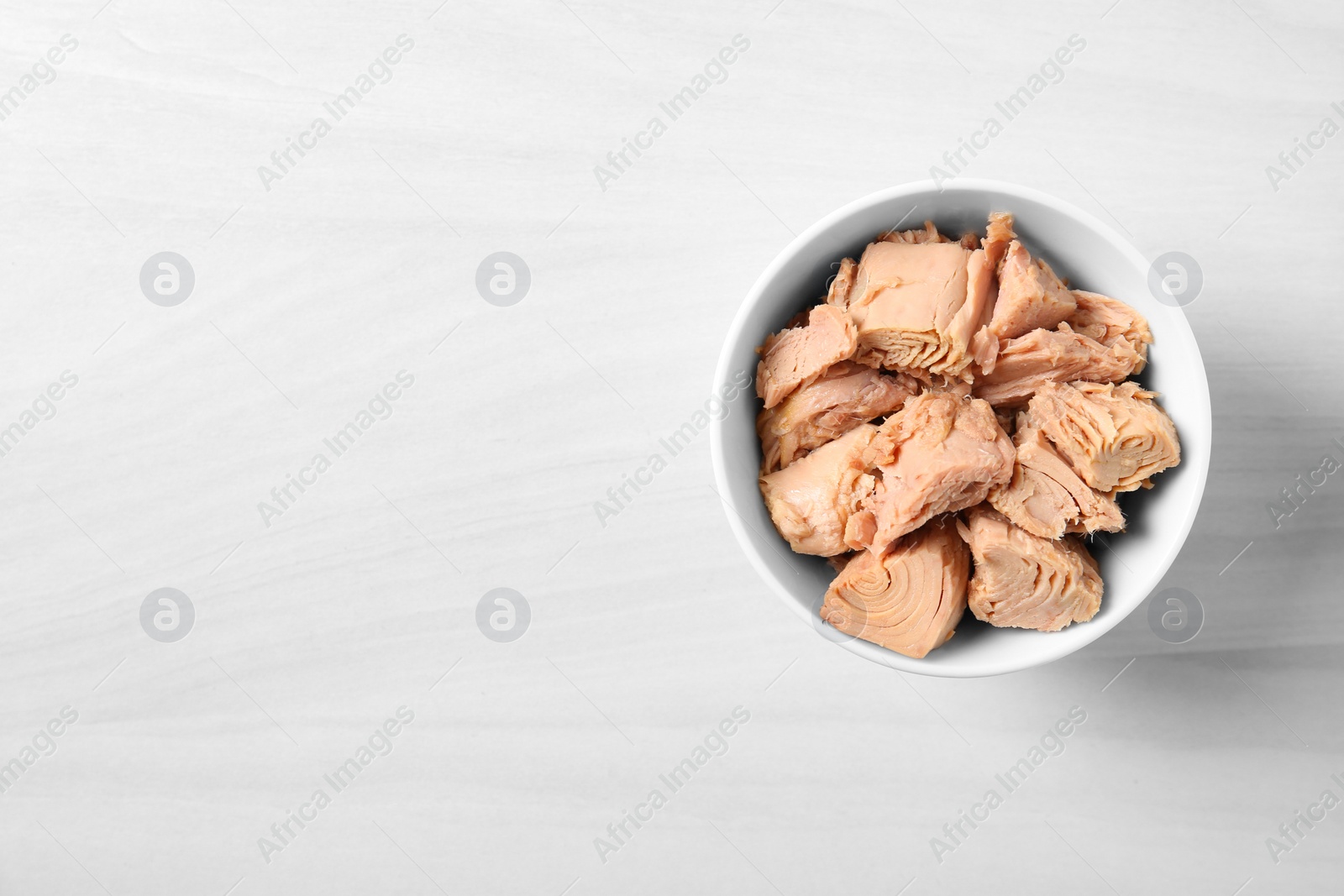 Photo of Bowl with canned tuna on light table, top view. Space for text