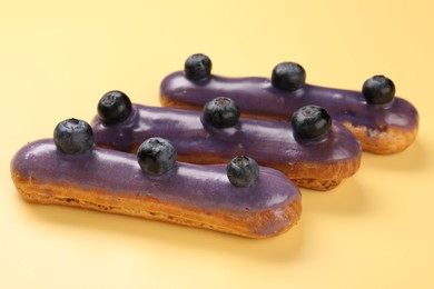 Photo of Delicious purple eclairs decorated with blueberries on yellow background