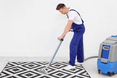 Male worker removing dirt from carpet with professional vacuum cleaner indoors