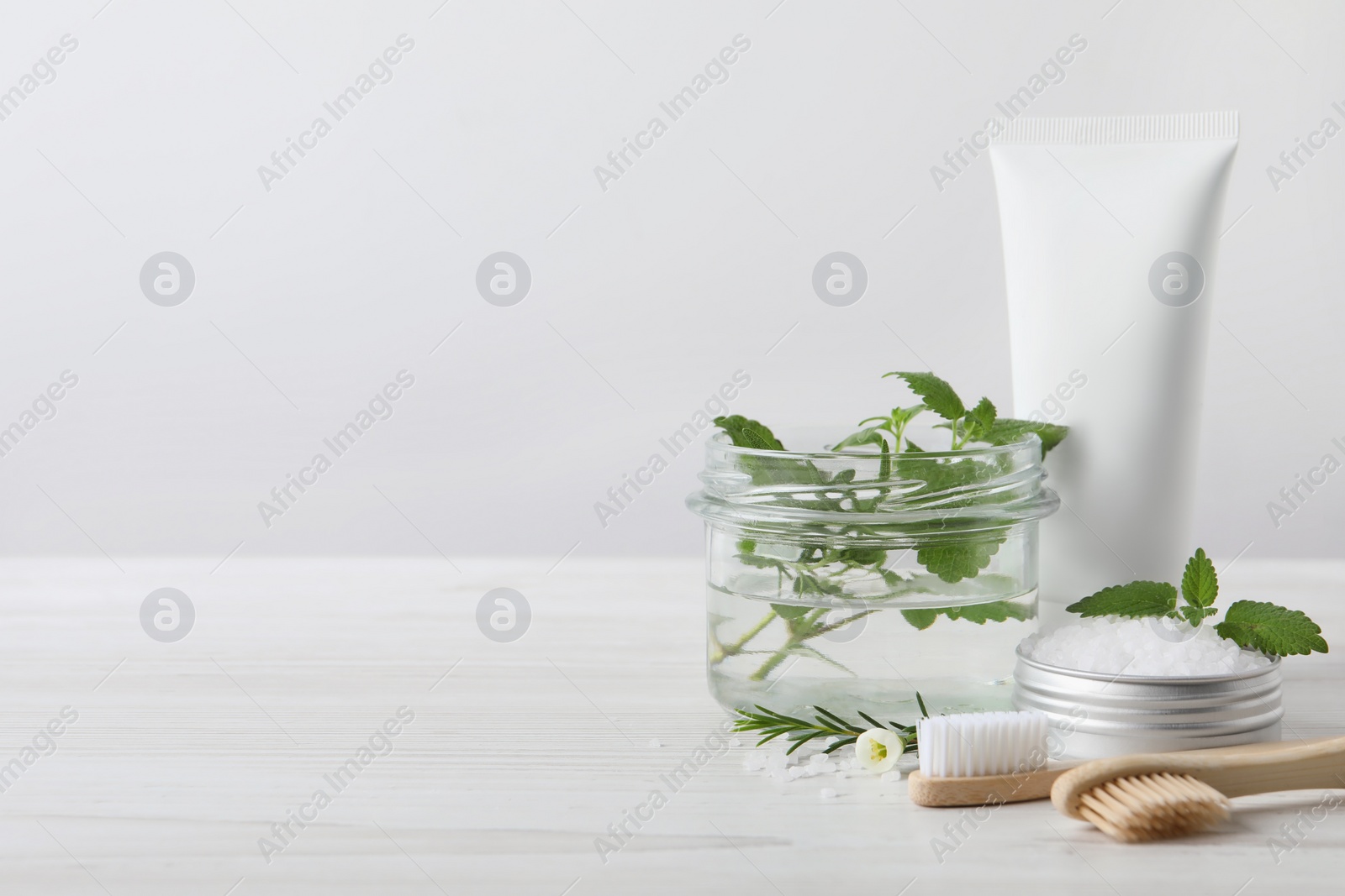 Photo of Toothbrushes, dental products and herbs on white wooden table. Space for text