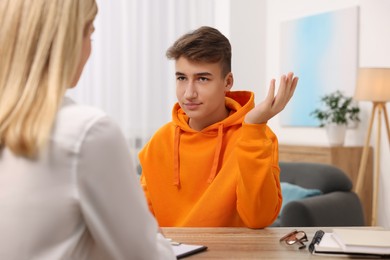 Psychologist working with teenage boy at table in office