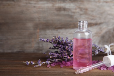Photo of Bottle with aromatic lavender oil on wooden table. Space for text