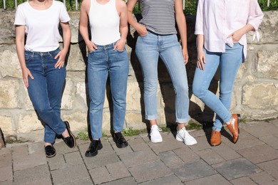 Photo of Women in stylish jeans near stone wall outdoors on sunny day, closeup