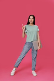 Young woman with modern laptop on pink background