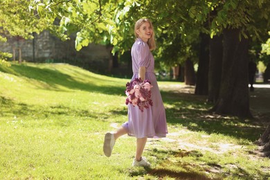 Beautiful woman with bouquet of spring flowers in park on sunny day