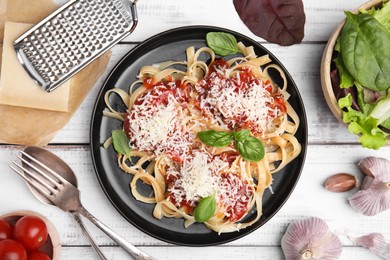 Delicious pasta with tomato sauce, basil and parmesan cheese on white wooden table, flat lay