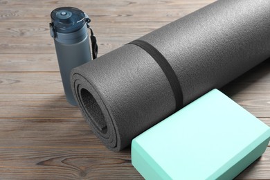 Photo of Exercise mat, yoga block and bottle of water on wooden floor