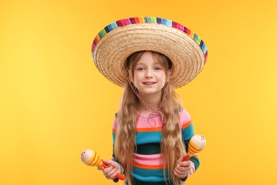 Photo of Cute girl in Mexican sombrero hat with maracas on orange background