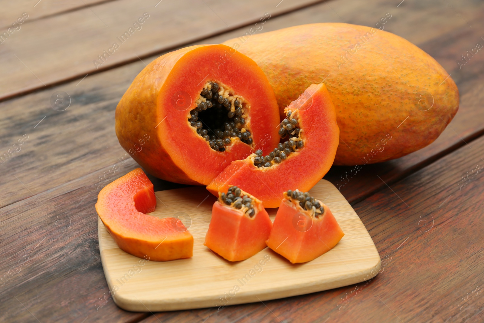 Photo of Ripe cut and whole papaya fruits on wooden table