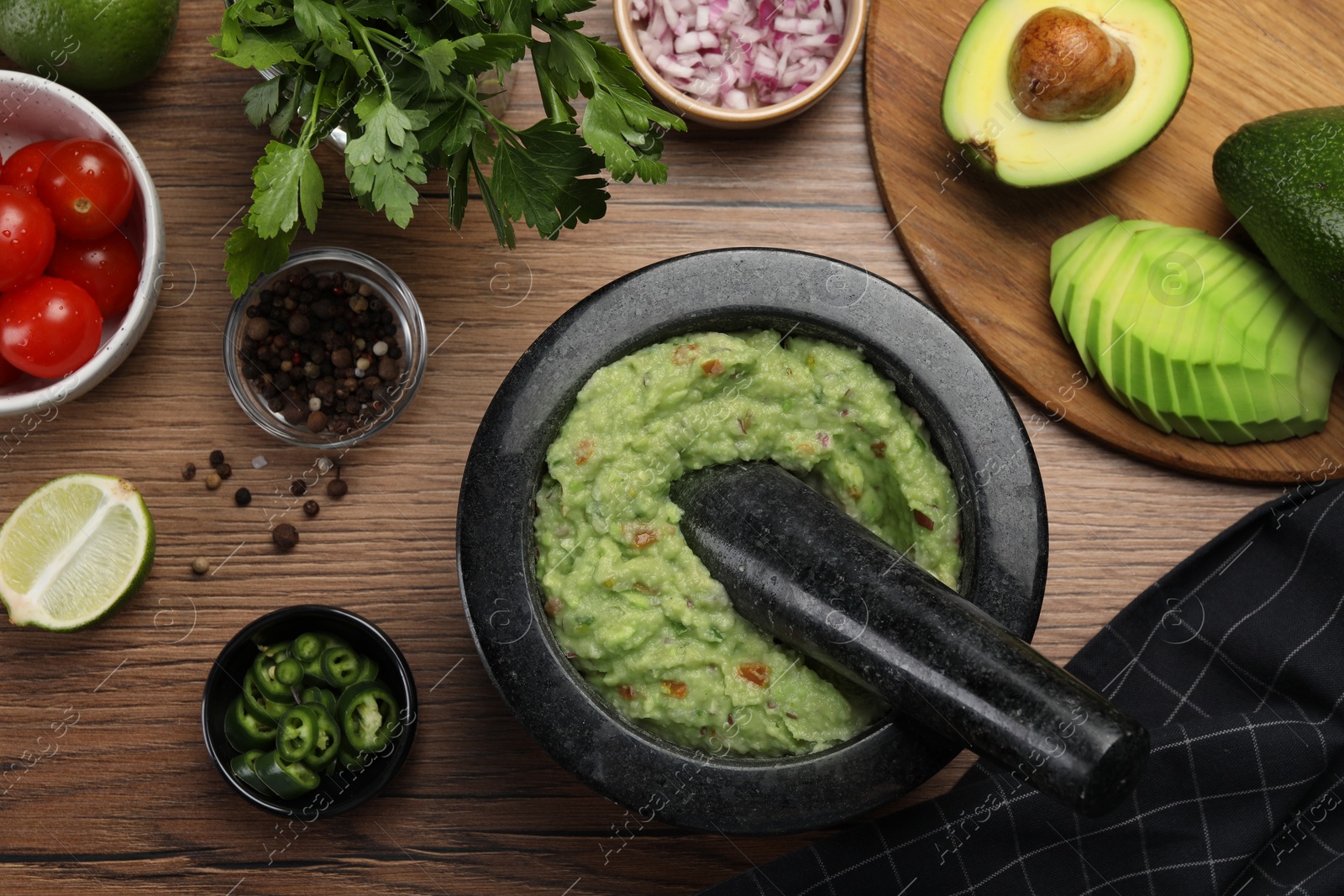 Photo of Delicious guacamole in mortar and ingredients on wooden table, flat lay