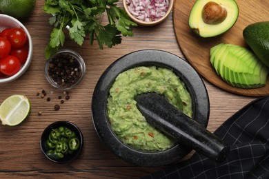 Photo of Delicious guacamole in mortar and ingredients on wooden table, flat lay