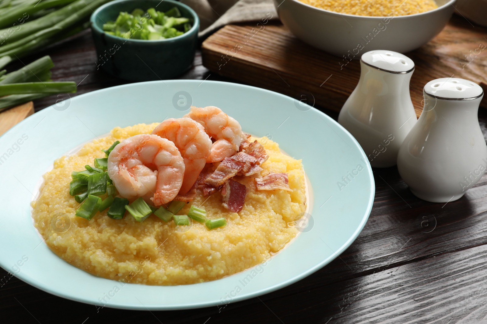 Photo of Plate with fresh tasty shrimps, bacon, grits and green onion on dark wooden table