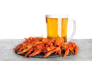 Delicious red boiled crayfishes and mug of beer on grey table against white background