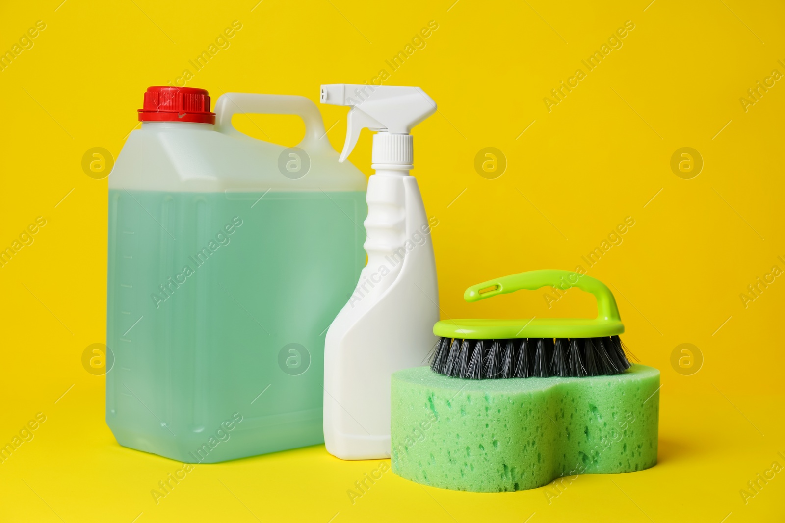 Photo of Bottles of detergents and tools on yellow background. Cleaning supplies