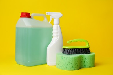 Photo of Bottles of detergents and tools on yellow background. Cleaning supplies