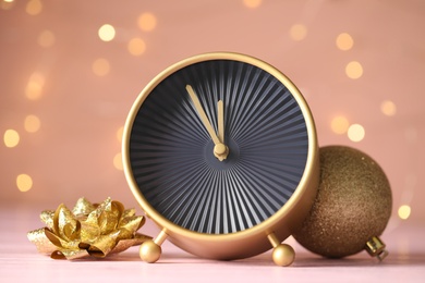 Stylish clock with decor on pink table against blurred Christmas lights, closeup. New Year countdown