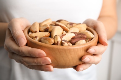 Photo of Woman holding bowl with Brazil nuts on blurred background, closeup
