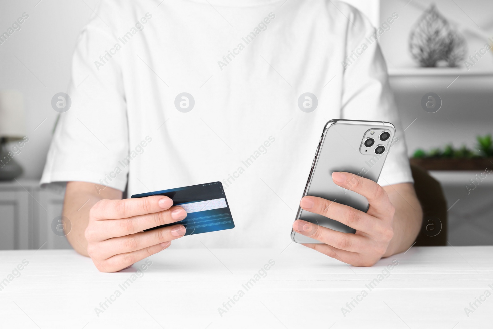 Photo of Online payment. Woman with smartphone and credit card at white table, closeup