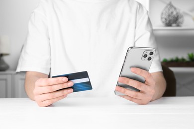 Photo of Online payment. Woman with smartphone and credit card at white table, closeup