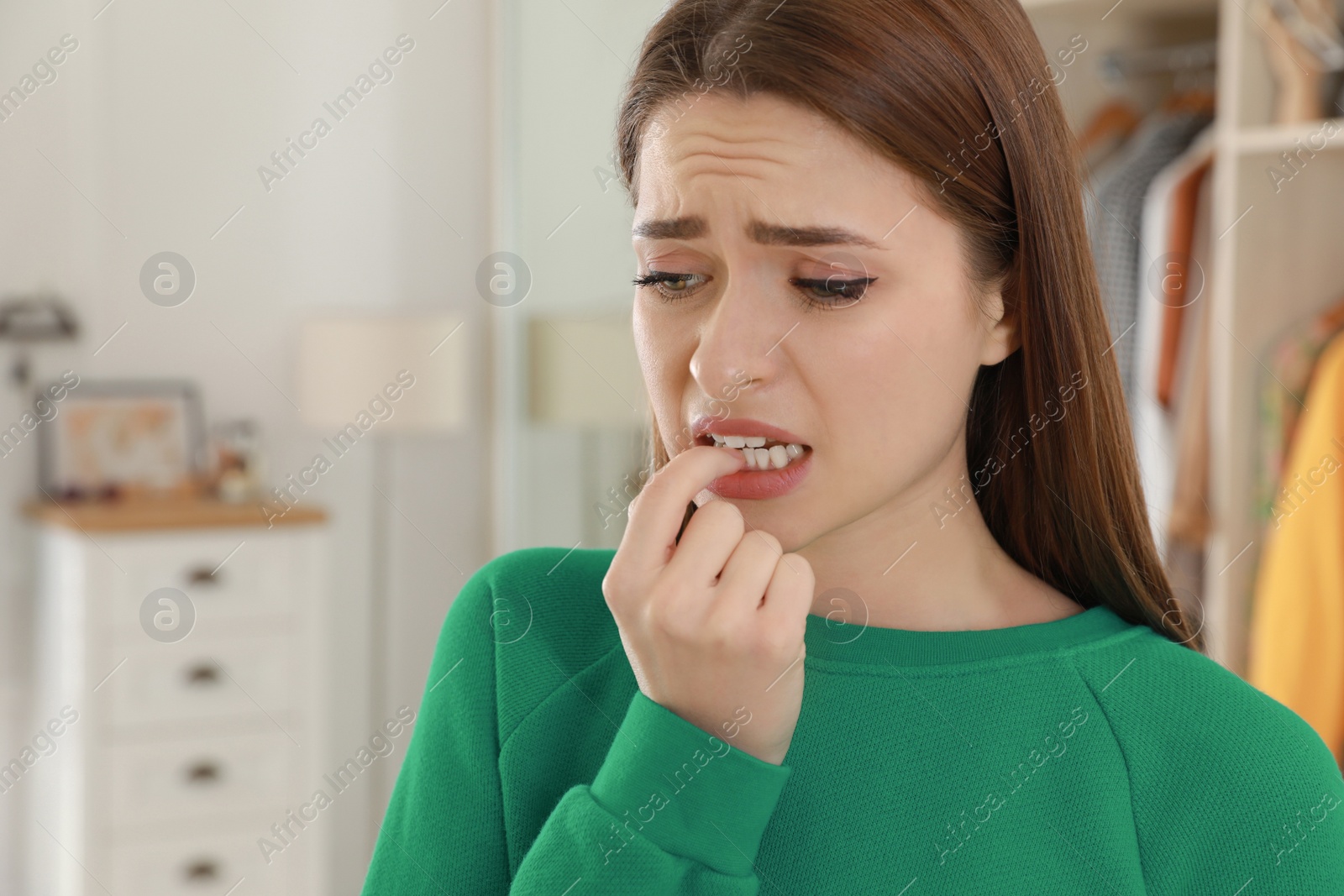 Photo of Young woman biting her nails at home. Space for text