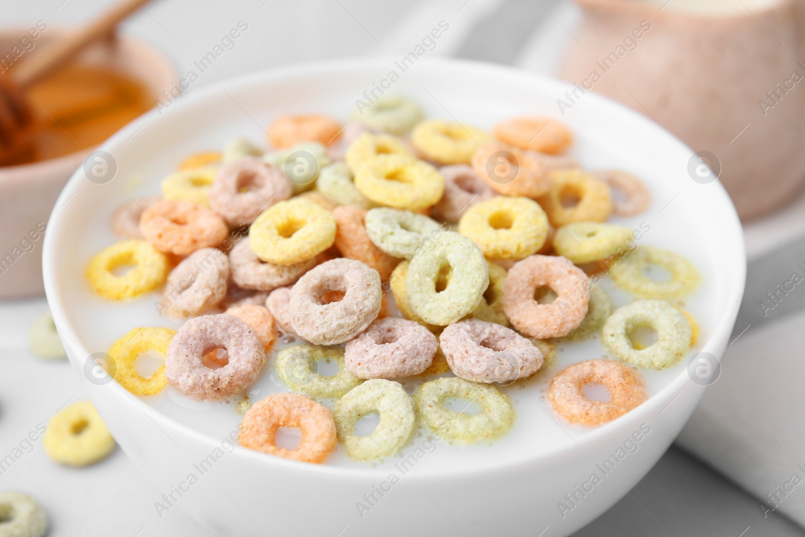 Photo of Cereal rings and milk in bowl on white table, closeup