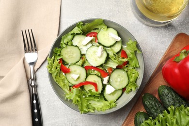 Photo of Delicious salad with cucumbers, red bell pepper and feta cheese in bowl served on light grey table, flat lay
