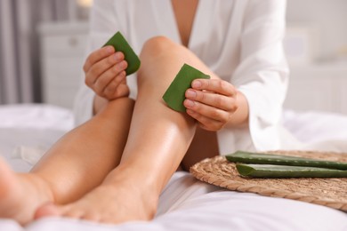 Photo of Young woman applying aloe gel from leaves onto her leg on bed, closeup