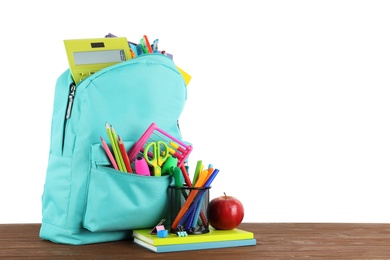 Bright backpack with school stationery on brown wooden table against white background, space for text