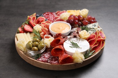 Photo of Wooden plate with different delicious snacks on grey table, closeup