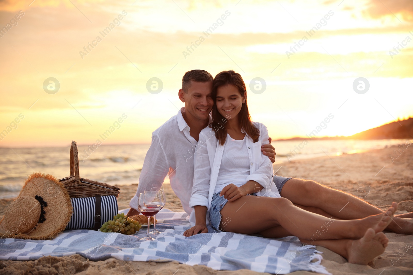 Photo of Lovely couple having romantic picnic on beach at sunset