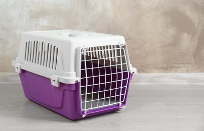 Photo of Violet pet carrier on floor near beige wall, space for text