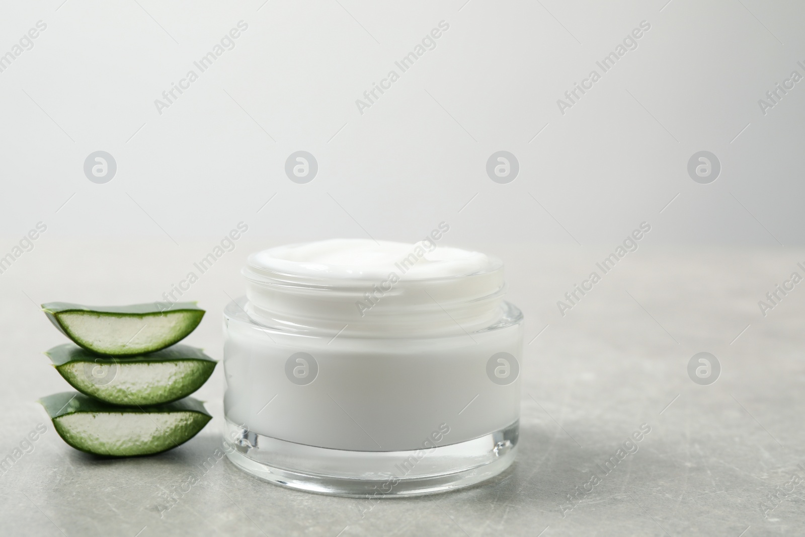 Photo of Open jar of cream and cut aloe on grey table. Organic cosmetics