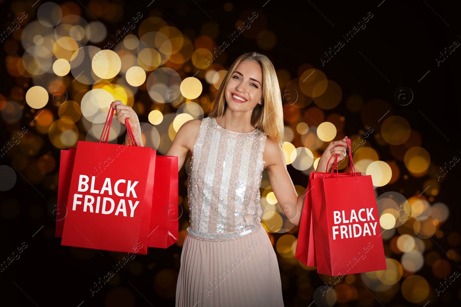 Image of Black Friday sale. Happy young woman with shopping bags on dark background, bokeh effect