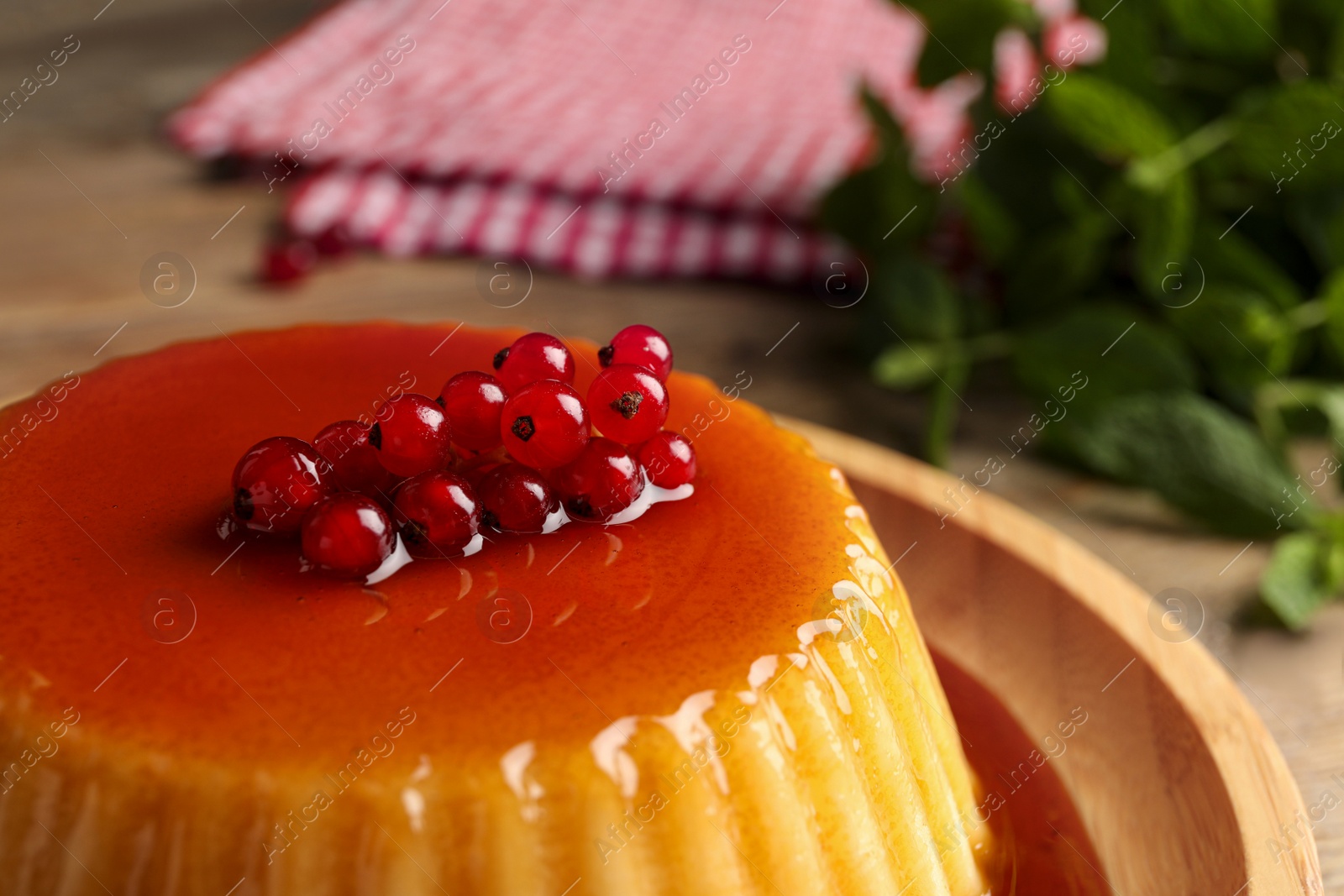 Photo of Delicious pudding with caramel and redcurrants on wooden table, closeup