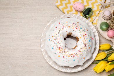Photo of Easter cake with sprinkles, painted eggs and tulips on white wooden table, flat lay. Space for text